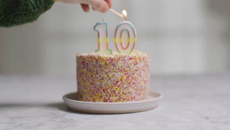 Studio-Shot-Birthday-Cake-Covered-With-Decorations-And-Candle-Celebrating-Tenth-Birthday-Being-Lit