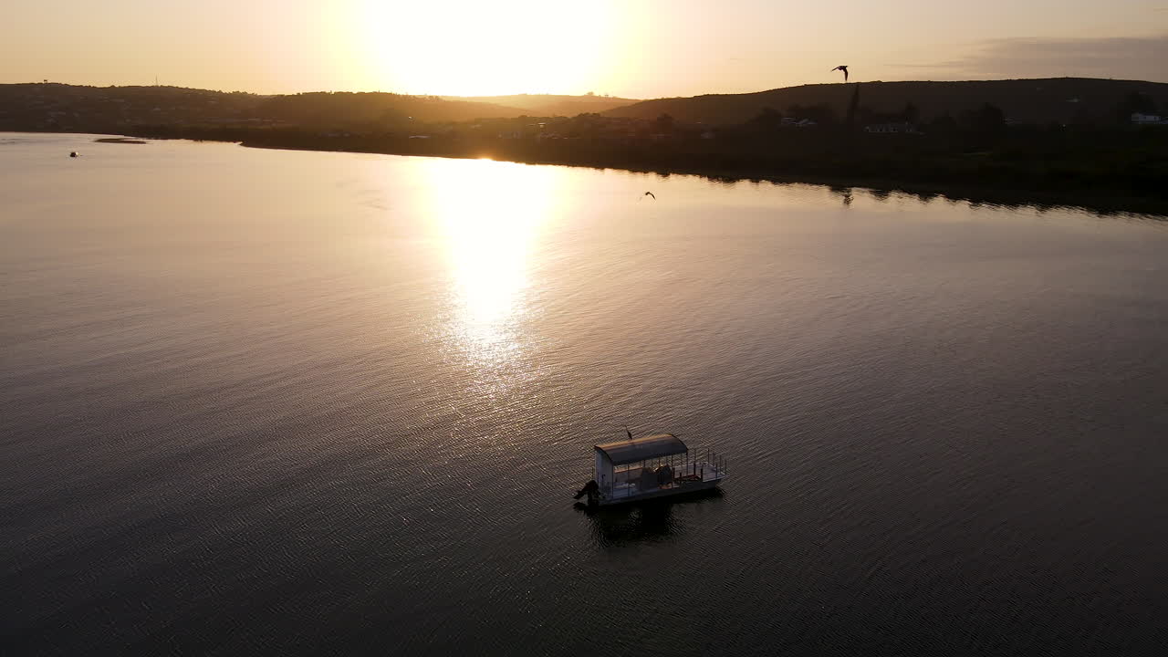 Ripresa panoramica con drone con allontanamento su una barca ancorata in un estuario - riflesso dorato del tramonto.