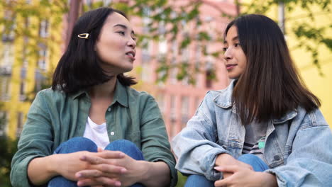 Two-Pretty-Young-Japanese-Girls-Sitting-And-Talking-Together-Outdoors