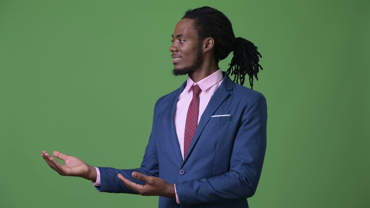 Young handsome African businessman with dreadlocks against green background