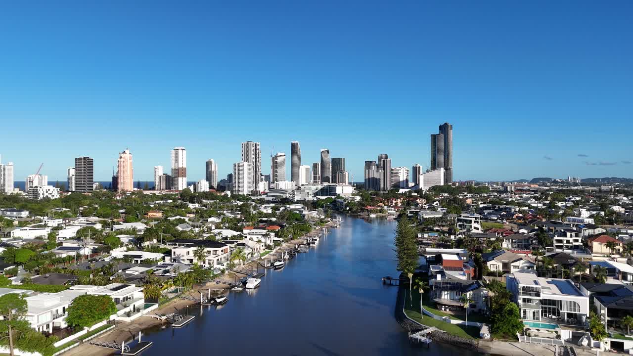 Drone footage captures Gold Coast's skyline, river, and residential areas under clear blue skies, showcasing urban and natural harmony