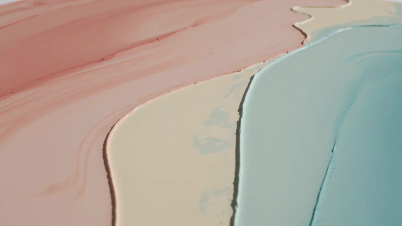 Cámara desplazándose revelando bandas de pintura rosa, beige y azul pálido asentándose en las crestas brillantes de un panel de estudio.