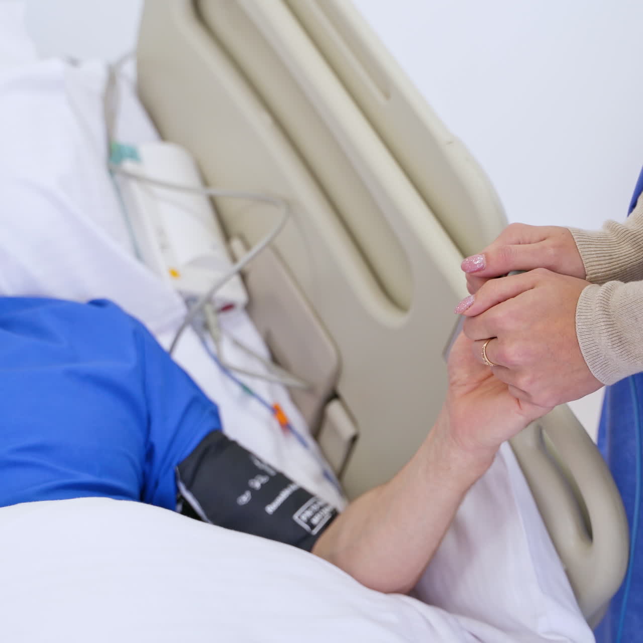 Close-up woman's hands supporting sick patient. Female visitor holds hands of her father in the hospital room. Senior male patient is laying in bed in clinic.