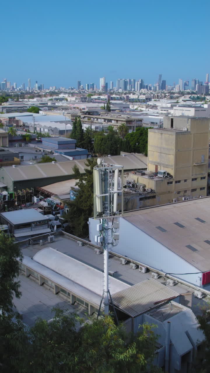 Telephone tower monopole antenna is hiding behind trees next to a factory in a modern industrial area - Vertical video