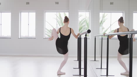 Caucasian-female-ballet-dancer-stretching-up-by-the-mirror-in-a-bright-studio