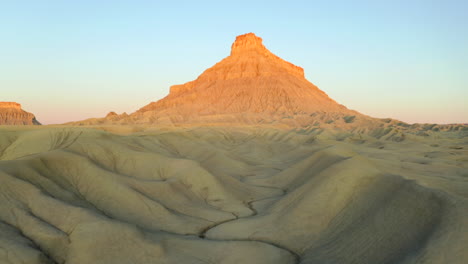 drone flying through canyon and dried up river bed towards factory butte at sunrise golden hour in utah