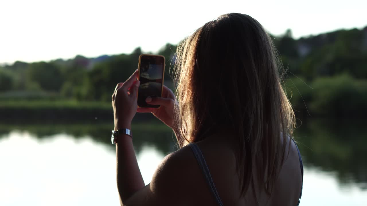 Toma de espaldas de una chica fotografiando un paisaje lacustre veraniego