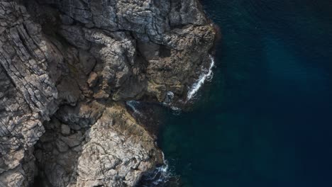 tiro de arriba hacia abajo de un dron en un acantilado rocoso con olas estrellándose contra él