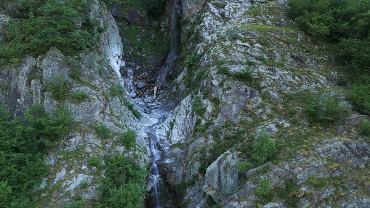 Small waterfall cascading down rugged, rocky gorge in Antrona Valley, Italian Alps, pristine nature and fresh water stream. Aerial drone ascending