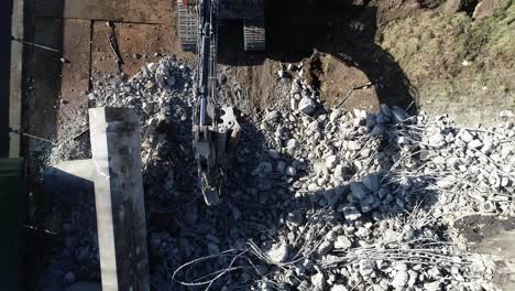 pull out drone shot of rubble at a construction site, there's an excavator standing at the rubble