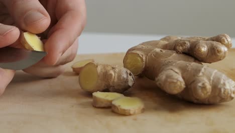 man peeling fresh ginger root on wooden cutting board, close up