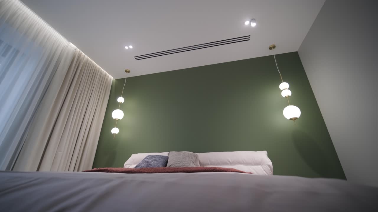 un dormitorio acogedor con una pared de acento verde, iluminación de colgante moderna, y una cama cómoda vestida con sábanas suaves