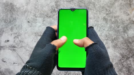 person holding a smartphone with a green screen