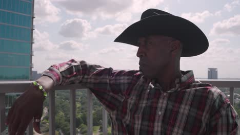 Toma-Panorámica-Izquierda-De-Un-Hombre-Negro-Con-Sombrero-De-Vaquero-Sentado-En-El-Balcón-Pensando