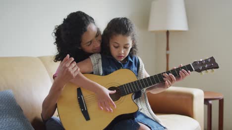 happy mixed race mother and daughter playing with guitar