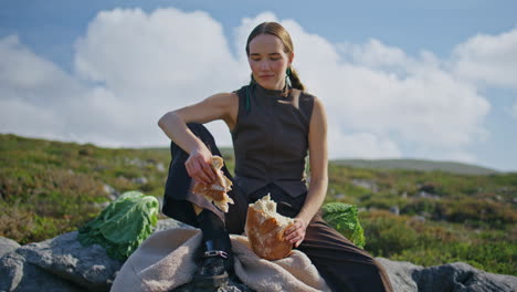 woman breaking homemade bread in sunlight. traveler enjoying picnic in mountains