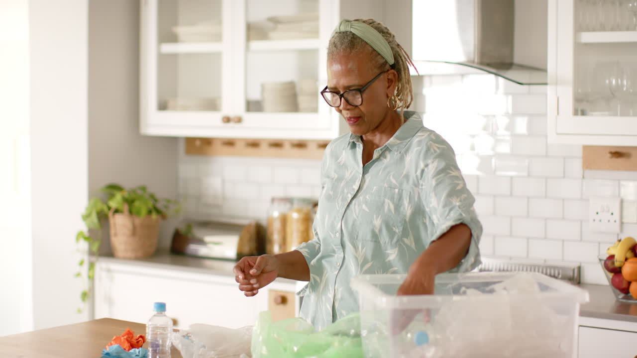 A senior African American woman is sorting recycling in kitchen