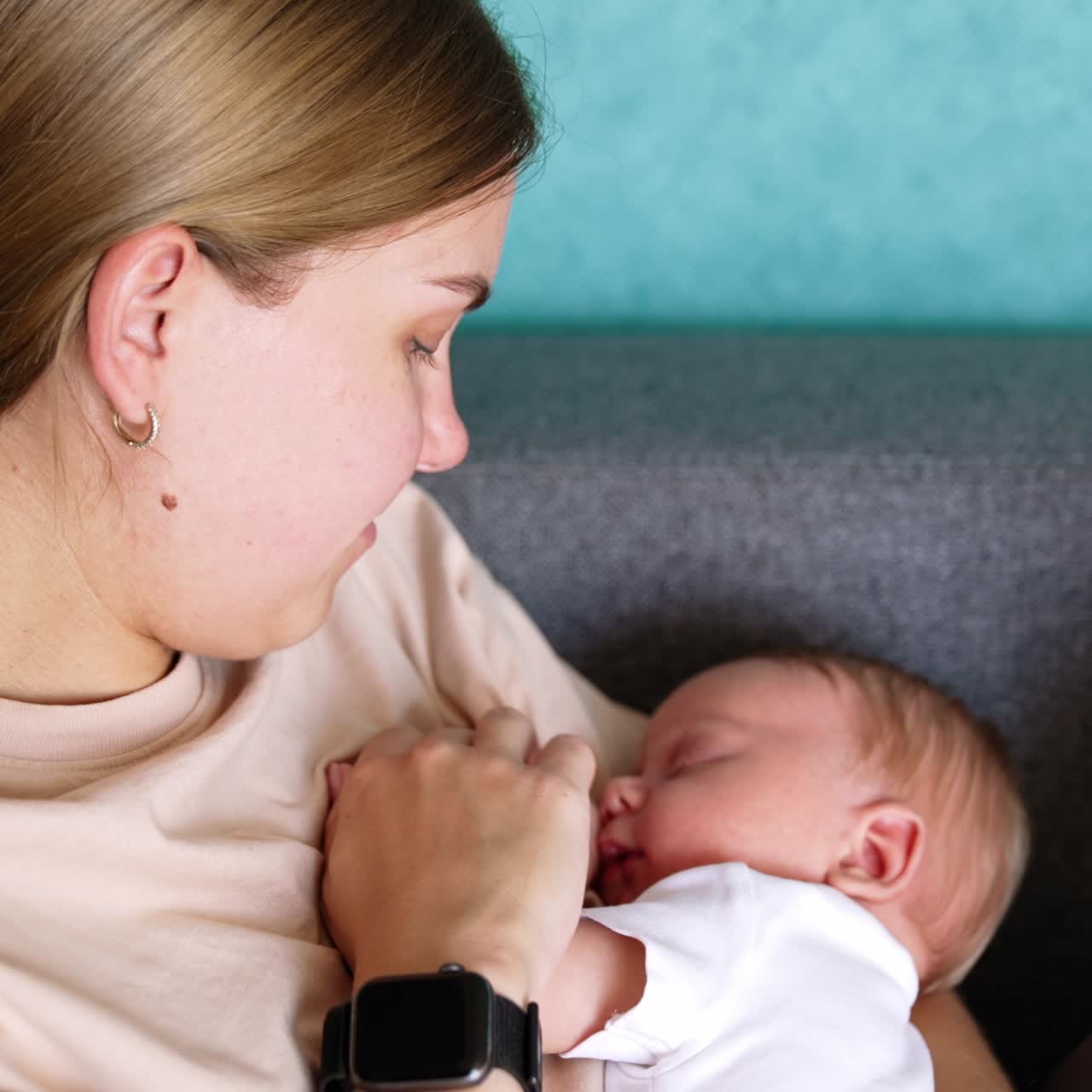 Blond Caucasian woman holding her sleeping newborn. Mom touches her child's ear tenderly. Close up