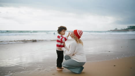 Mamá-Hijo-Descansando-Junto-Al-Mar-El-Fin-De-Semana-De-Otoño.-Adorable-Niño-Tocando-A-Su-Madre