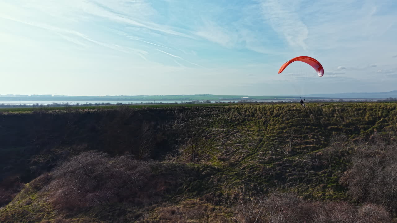 En paraglider svæver over grønne marker under en blå himmel på landet på en solrig dag.