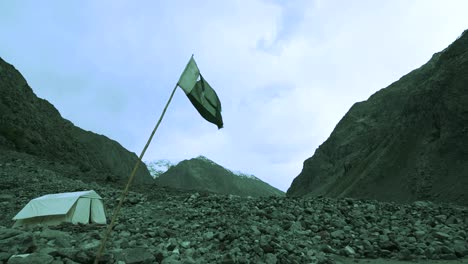 torn flag of pakistan going down, falpping through winds in the middle of mountains