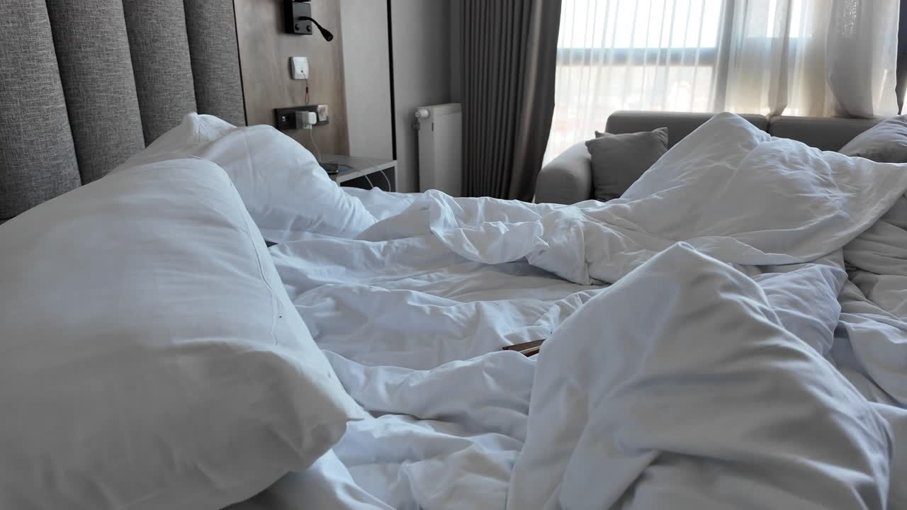 Seseorang mengambil pakaian dari tempat tidur yang berantakan dan belum dirapikan di kamar hotel.