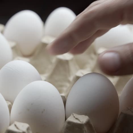 close view of a farmer taking eggs from a pile and placing them into a carton to be sold