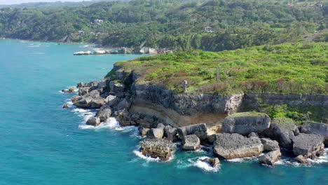 small waves from clear blue atlantic ocean crash against a picturesque grassy cliff, aerial pullback drone shot