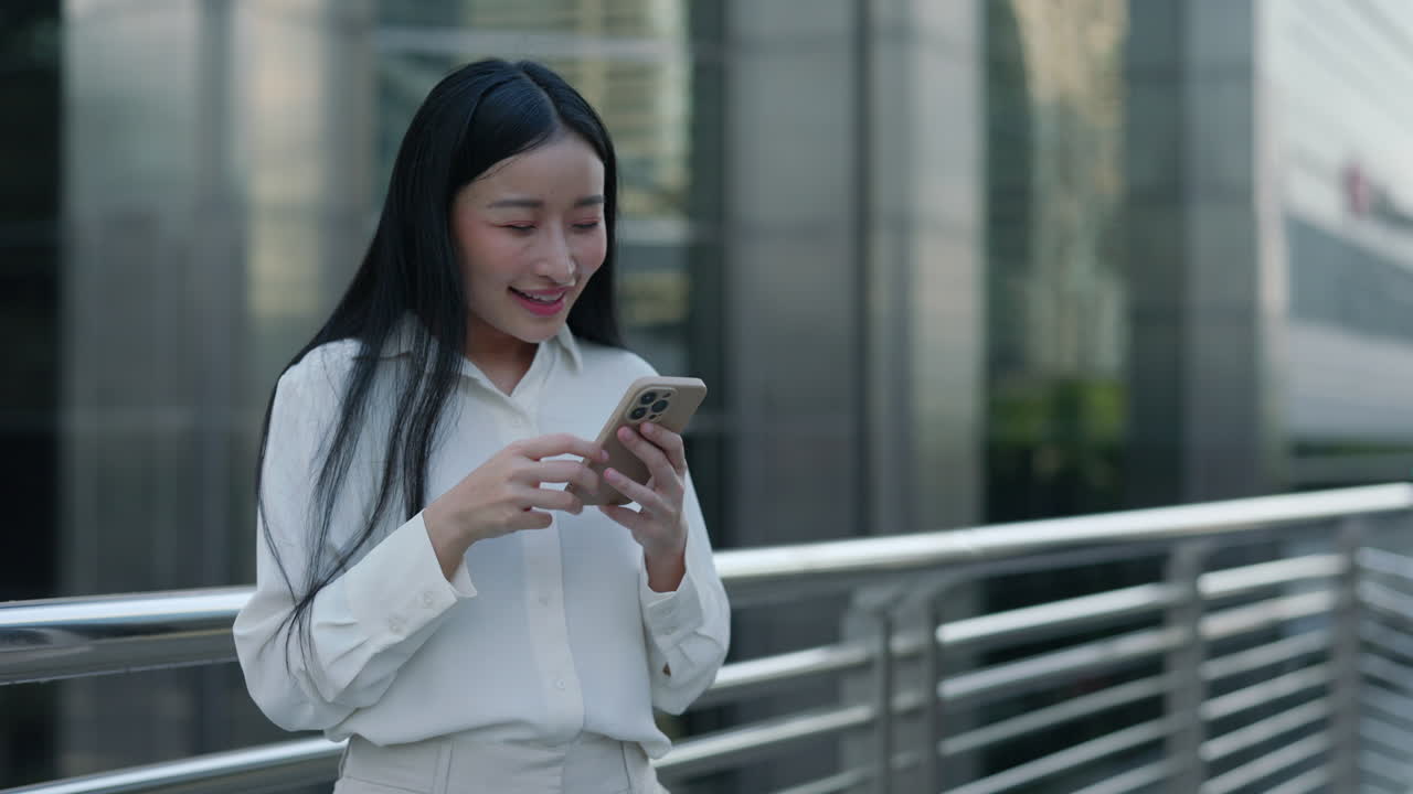 Happy Asian Woman Celebrating Success While Using Smartphone in City