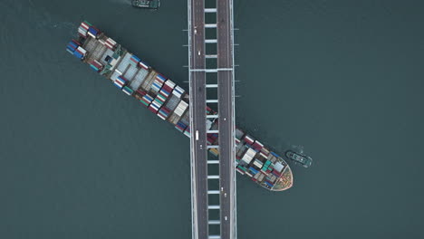 large freight ship passing under suspension bridge high-altitude top-down drone shot