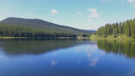 peppers lake with glass like water and surrounded by a vast evergreen forest is flown over to reveal the rocky mountains in alberta canada on a sunny summer day