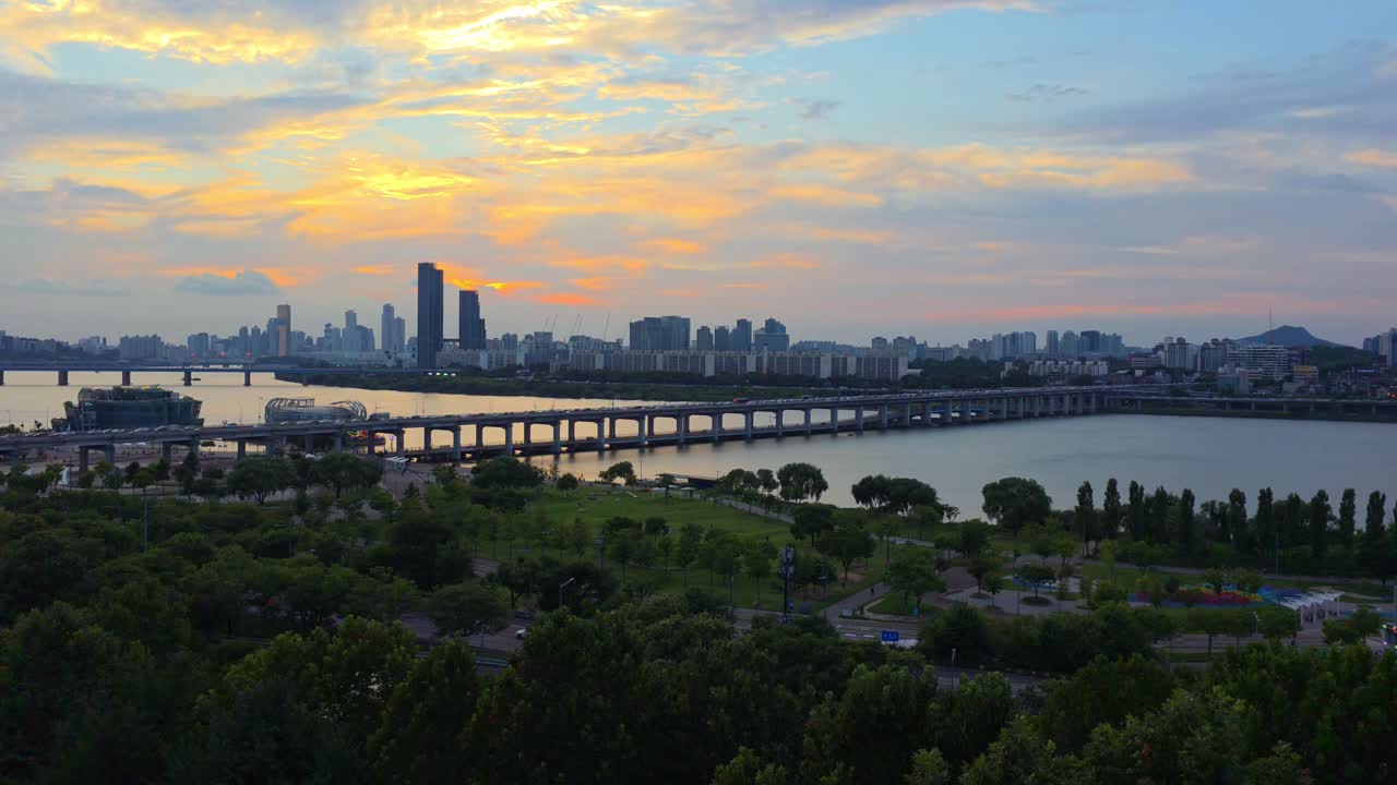 Seoul cityscape with Iconic Banpo Bridge spanning the Hangang River, with city traffic moving across as sky glows with warm colors of a beautiful summer sunset - static high-angle, real-time video