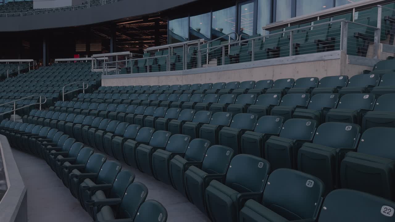 Lenta e costante panoramica attraverso file di sedili vuoti dello stadio, ringhiere e area di passaggio sotto la luce del giorno.