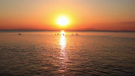 wide view of the silhouettes of people swimming and enjoying the summer sunset in koh sdach island in cambodia, candid carefree moment