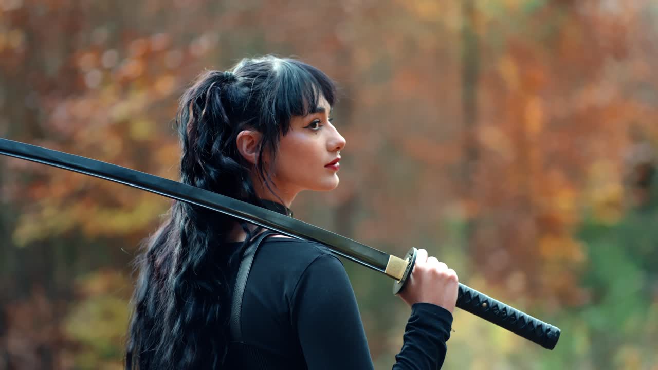 hermosa chica con cabello largo en un traje negro sostiene una katana japonesa y mira hacia atrás a la cámara sobre su hombro