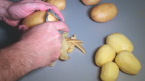 slow motion of male hands peeling potatoes with kitchen peeler, man at domestic work, cooking