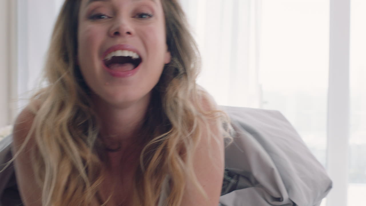 침대에서 놀고 있는 아름다운 여성이 담요  ⁇ 에 숨어서 집에서 즐거운 아침을 즐기고 있습니다.