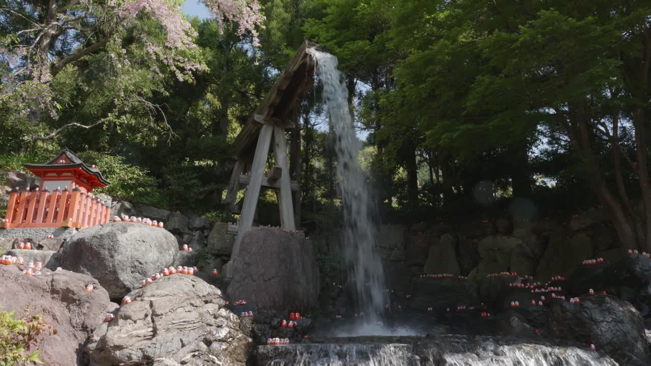 Water falling into a pond surrounded by small red daruma dolls on a sunny day at Katsuoji Temple, Osaka. Japan