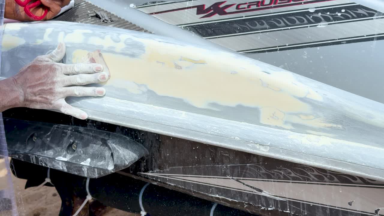 Close-up shot of a worker's hand sanding white filler on a boat in Phuket