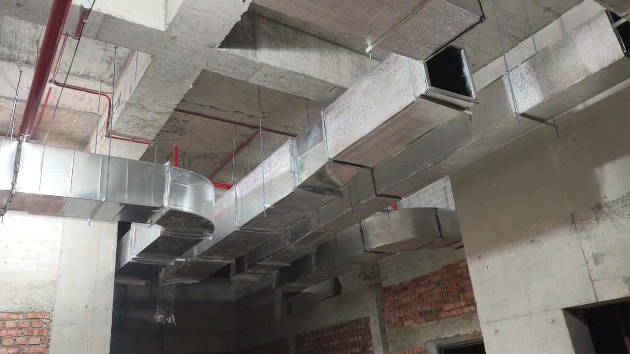 HVAC air ducts undergo installation at an active construction site. Wrapped in silver insulation, the unfinished network prepares to distribute cool airflow across the modern indoor space.
