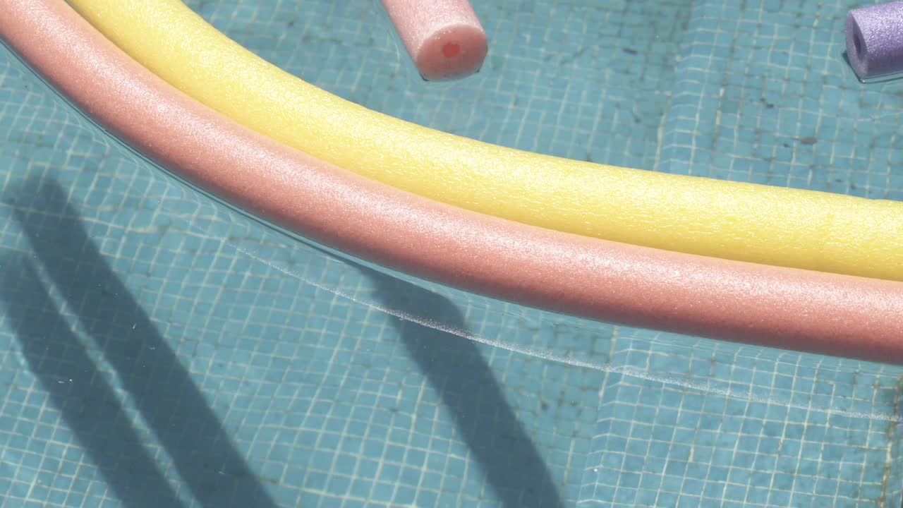 Two colorful pool noodles are floating on the surface of a dirty swimming pool, highlighting the need for cleaning and maintenance with some rubbish in the water