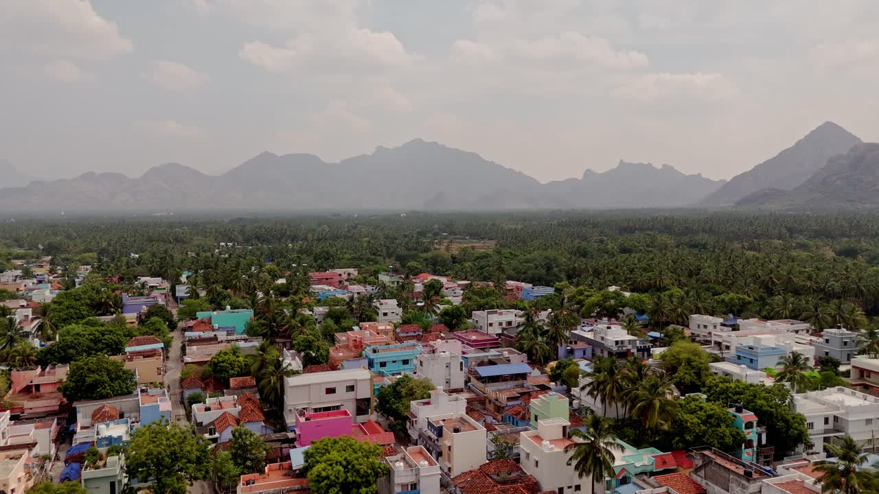 Drone view of hazy hills due to fog with rural colorful houses in foreground in between a forest area.