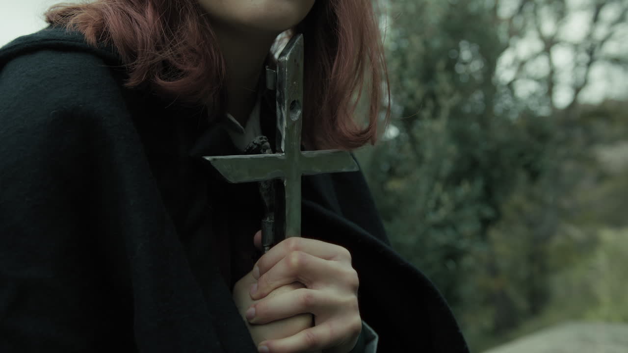 mujer reza sentada en el prado con el crucifijo de jesucristo en sus manos