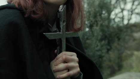 woman prays sitting in the meadow with crucifix of jesus christ in her hands