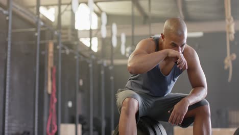 hombre biracial cansado sentado en una barra descansando después de levantar pesas en el gimnasio, cámara lenta, espacio de copia