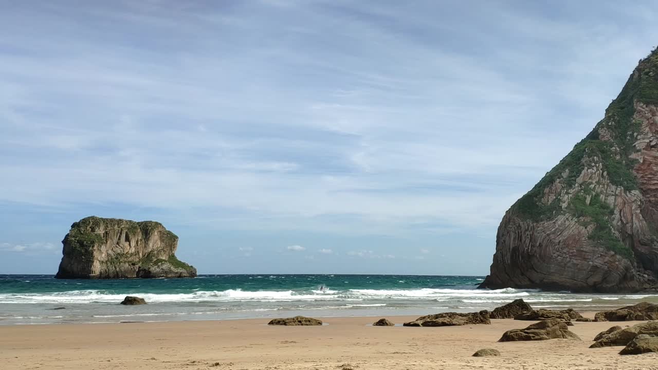 Beach view of Castro Ballota Islet from Ballota Beach in Asturias, showcasing the coastline and clear skies