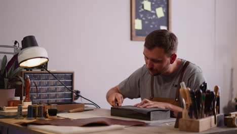 bearded master sharpens knife with sandpaper in shop