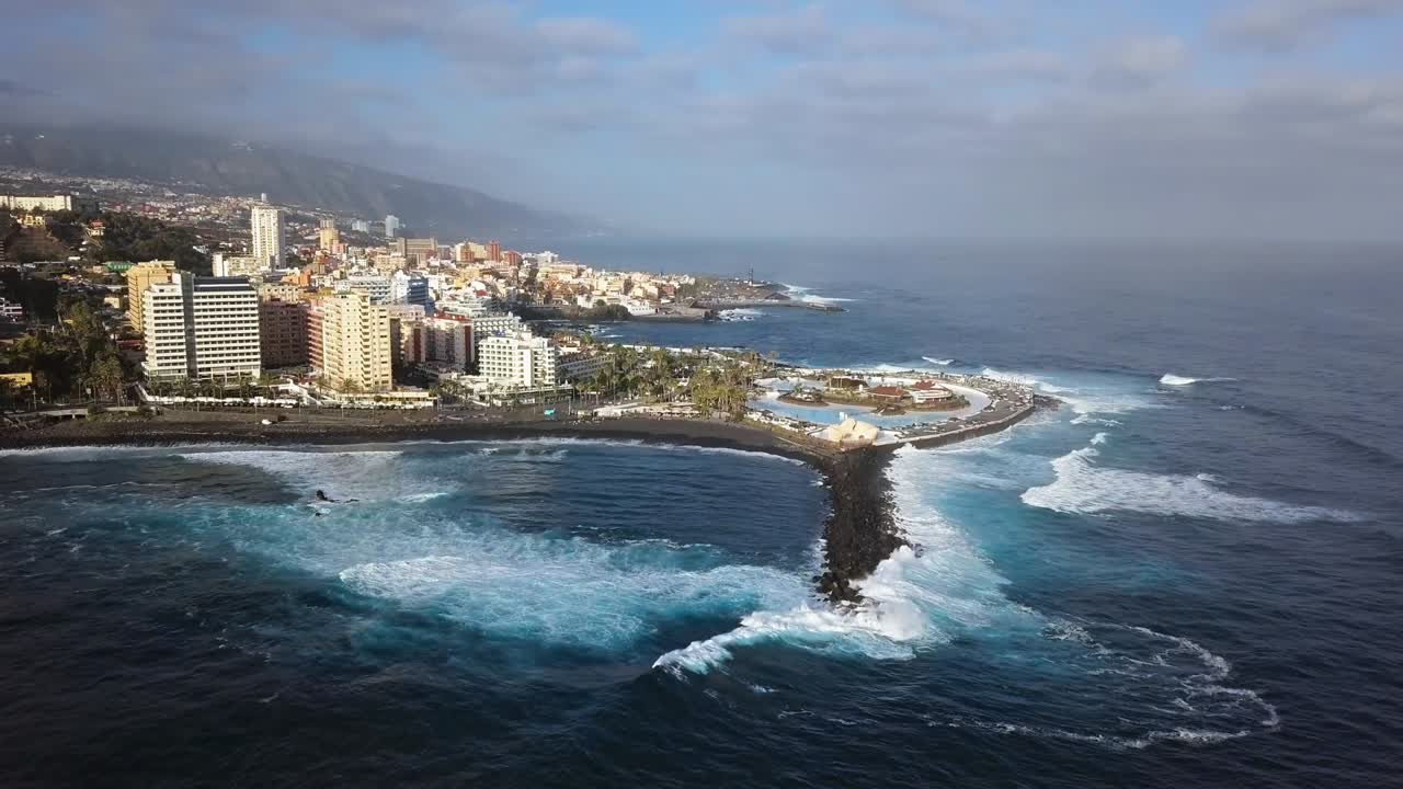 Panorama aéreo de los complejos turísticos y piscinas de Puerto de la Cruz rodeados por las olas del mar, Tenerife, Islas Canarias, España