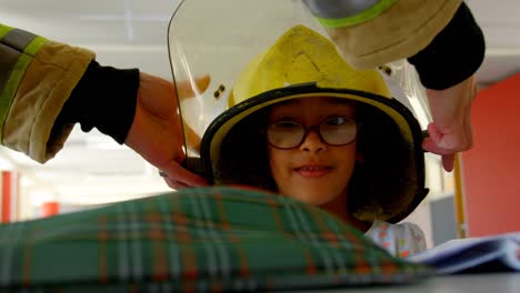Firefighter-helping-African-American-schoolgirl-by-putting-helmet-on-her-head-in-classroom-at-school