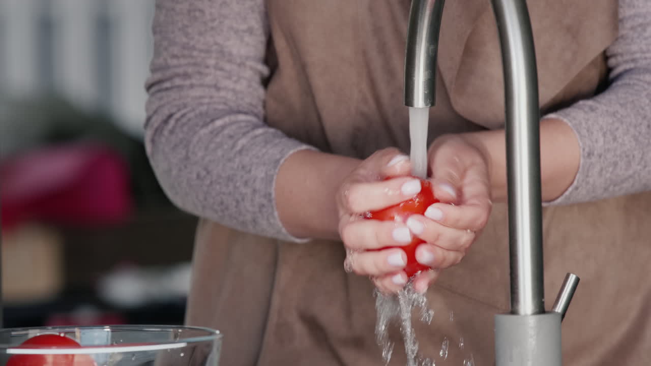 한 여성이 수도꼭지에서 나오는 물줄기 아래에서 토마토를 씻는다 1